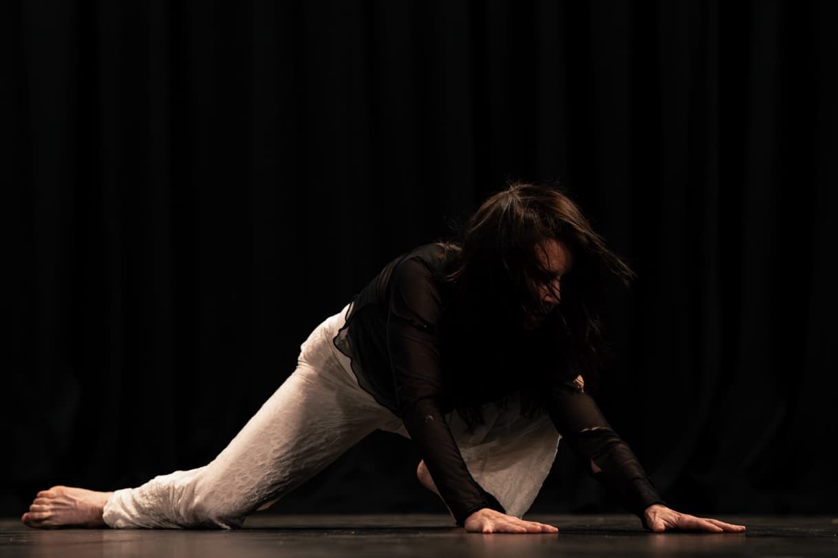 Wendy McPhee performing Reimagining Jean, low to the ground on a dark stage.